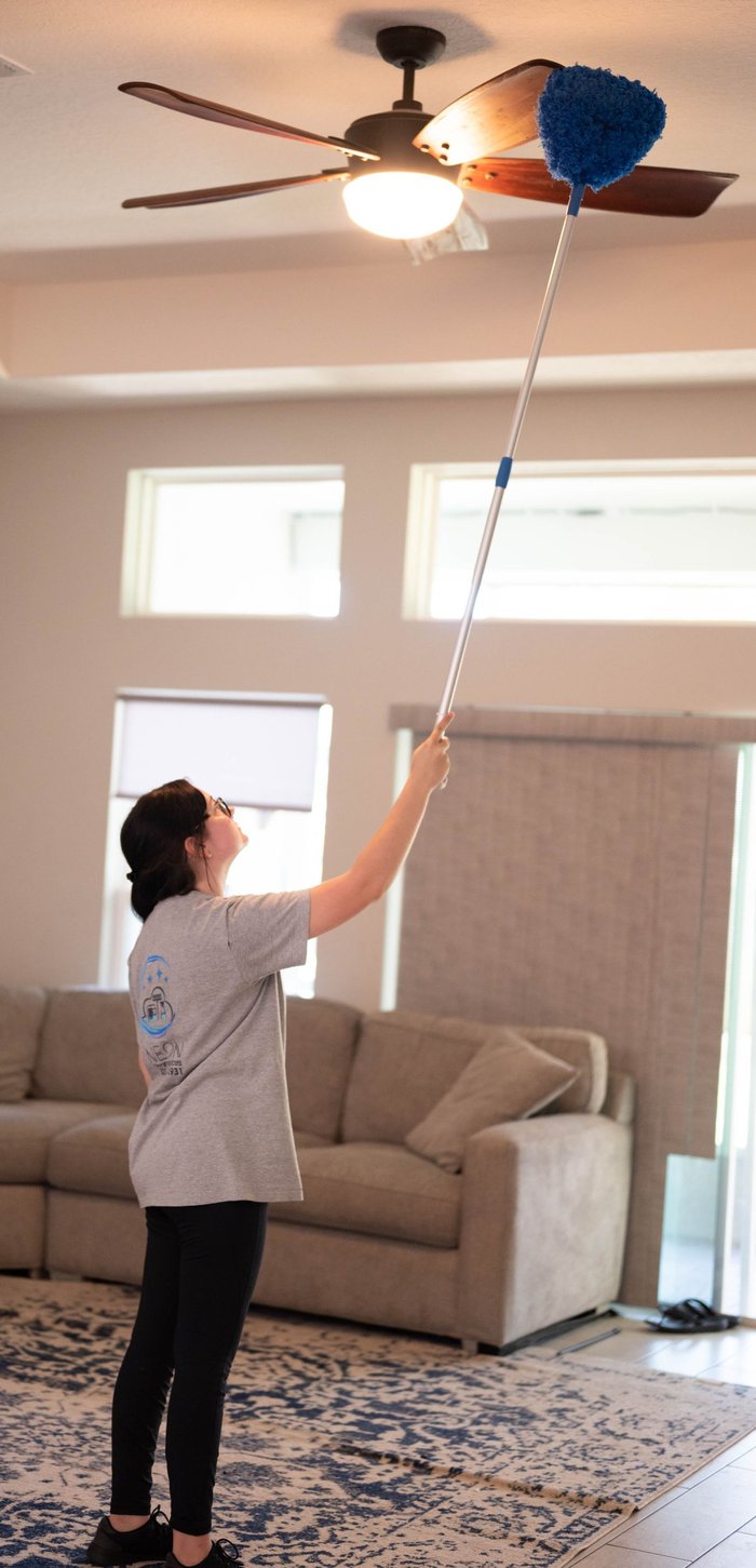 Neon Cleaning Services team member dusting a ceiling fan in a bright Melbourne, FL living room