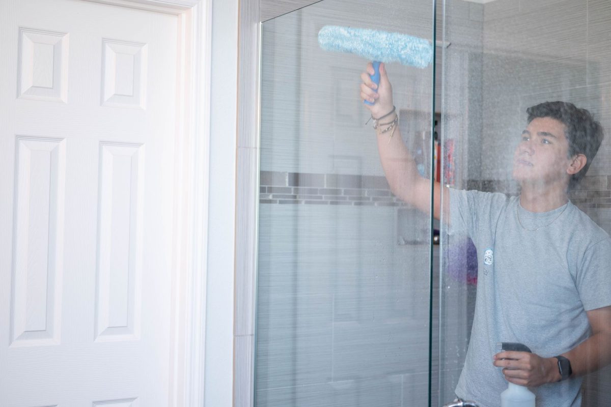 Neon Cleaning Services team member cleaning a glass shower door
